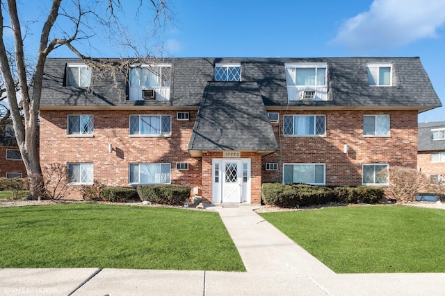 view of front of home featuring a shingled roof, mansard roof, a front lawn, and brick siding