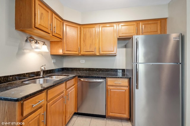 kitchen featuring appliances with stainless steel finishes, brown cabinets, a sink, and dark stone countertops