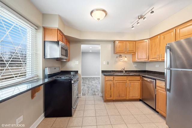 kitchen featuring light tile patterned floors, brown cabinetry, appliances with stainless steel finishes, dark stone countertops, and a sink