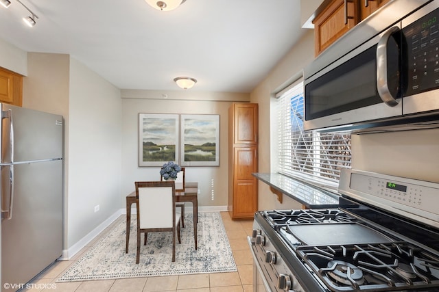 kitchen featuring baseboards, appliances with stainless steel finishes, brown cabinets, and light tile patterned flooring