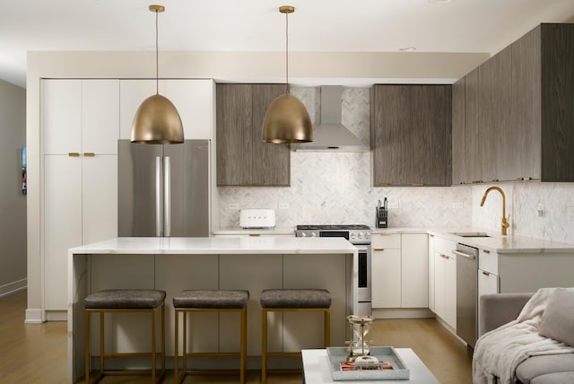 kitchen with stainless steel appliances, a sink, backsplash, wall chimney exhaust hood, and a kitchen bar