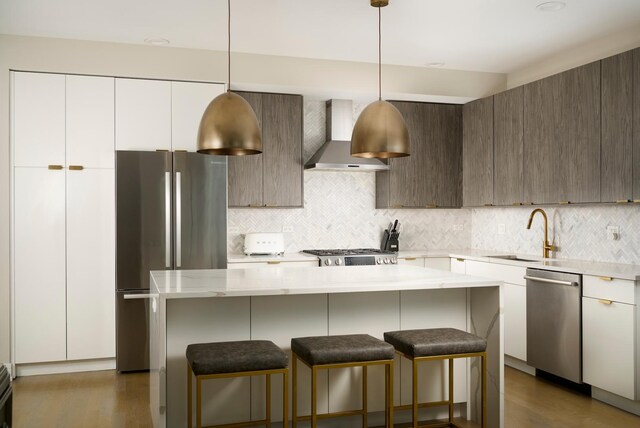 kitchen with a breakfast bar, stainless steel appliances, decorative backsplash, a sink, and wall chimney range hood