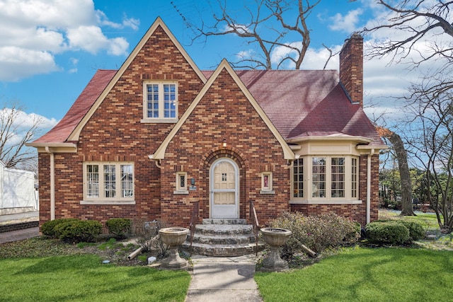 tudor home with a front yard, brick siding, and a chimney