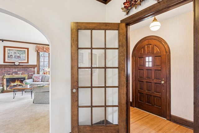 foyer with light carpet, arched walkways, a fireplace, and light wood-style flooring