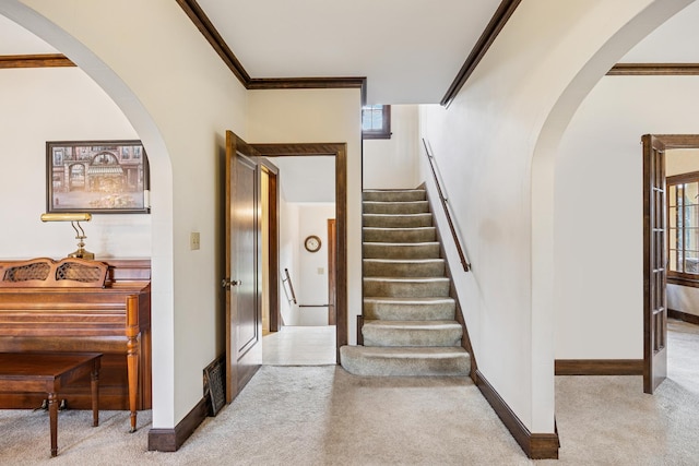 staircase with crown molding, baseboards, arched walkways, and carpet