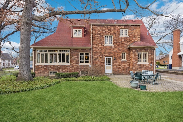 back of property featuring brick siding, roof with shingles, a patio area, and a lawn