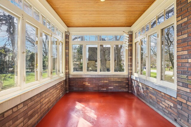 unfurnished sunroom with concrete flooring, brick wall, and wood ceiling