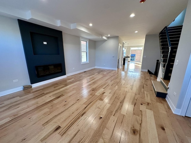 unfurnished living room with a large fireplace, baseboards, stairs, light wood-type flooring, and recessed lighting