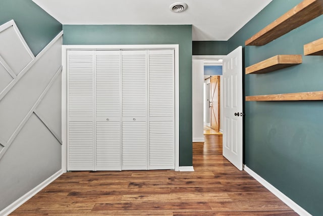 unfurnished bedroom featuring baseboards, a closet, visible vents, and dark wood-type flooring