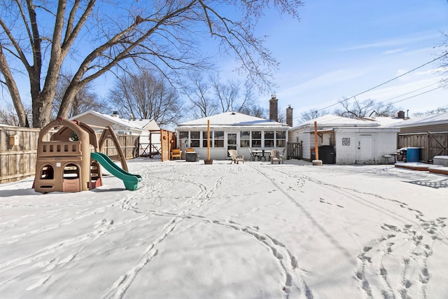 snow covered house with a sunroom, a playground, fence, and a chimney