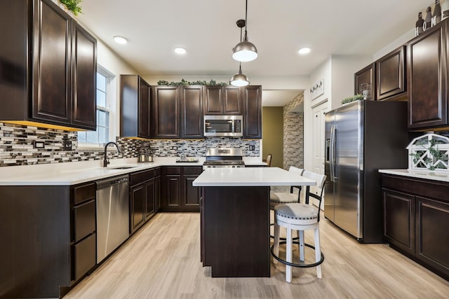 kitchen featuring a breakfast bar area, stainless steel appliances, backsplash, a sink, and dark brown cabinets