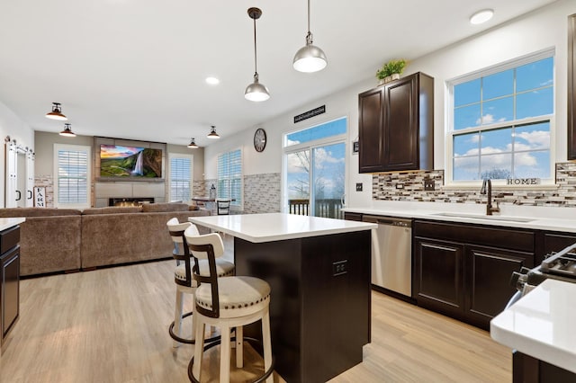 kitchen featuring a breakfast bar, stainless steel dishwasher, open floor plan, a sink, and dark brown cabinets