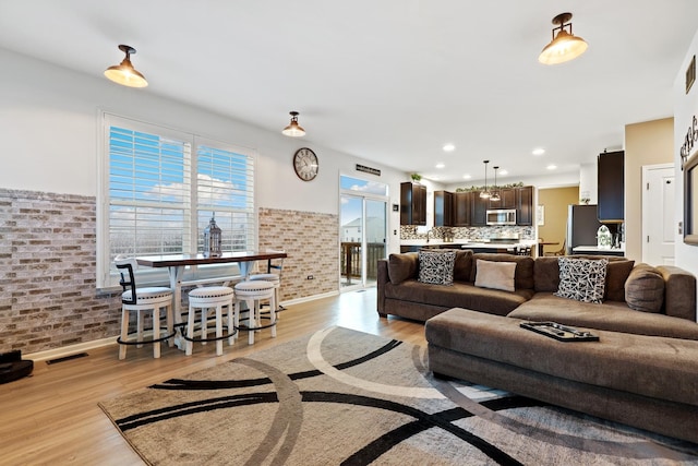 living area with brick wall, light wood finished floors, visible vents, and recessed lighting