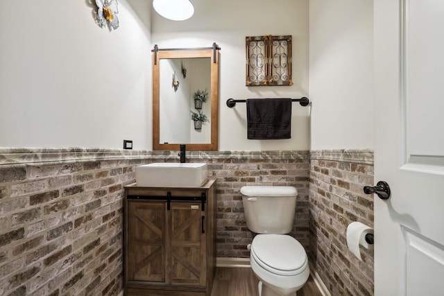 bathroom with toilet, wainscoting, brick wall, and vanity