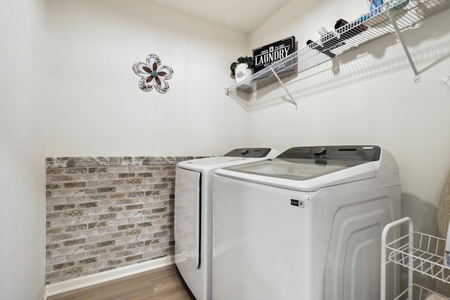 washroom featuring laundry area, baseboards, brick wall, wood finished floors, and independent washer and dryer