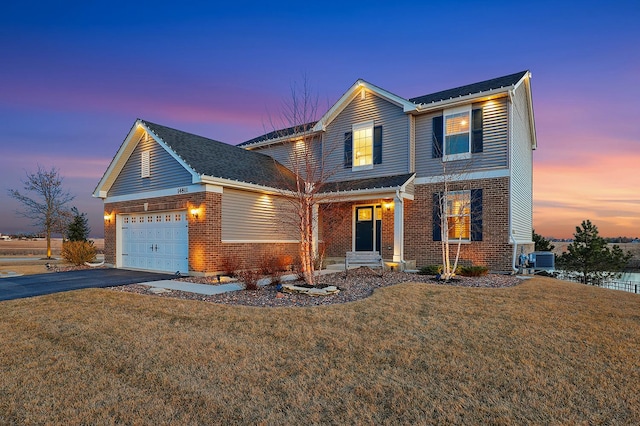 traditional-style house with aphalt driveway, brick siding, a garage, and a front lawn