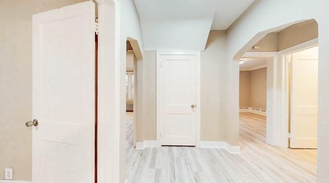 hallway with arched walkways, light wood finished floors, and baseboards