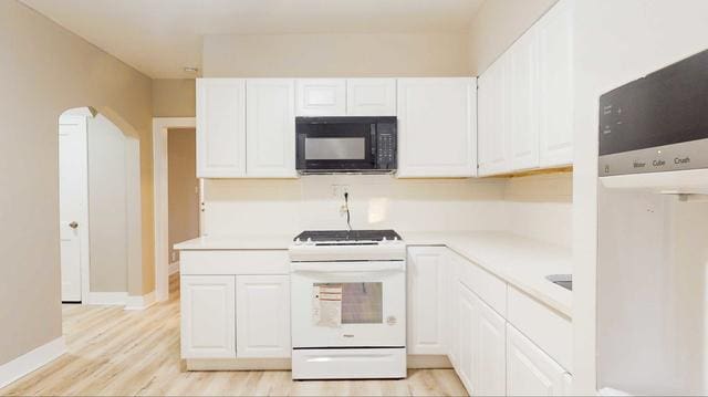 kitchen with black microwave, white range with gas stovetop, arched walkways, light countertops, and white cabinetry