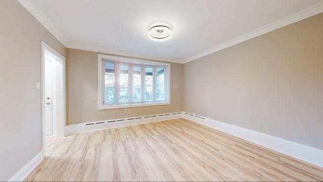 unfurnished room featuring a baseboard radiator, baseboards, crown molding, and light wood finished floors