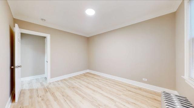 unfurnished room featuring radiator, light wood-style flooring, and baseboards