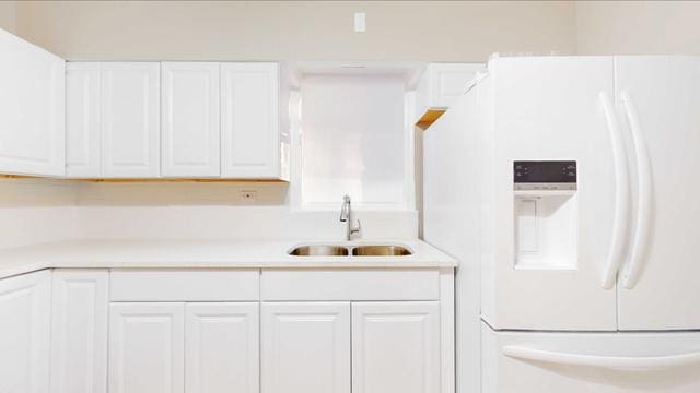 kitchen featuring white fridge with ice dispenser, light countertops, white cabinets, and a sink