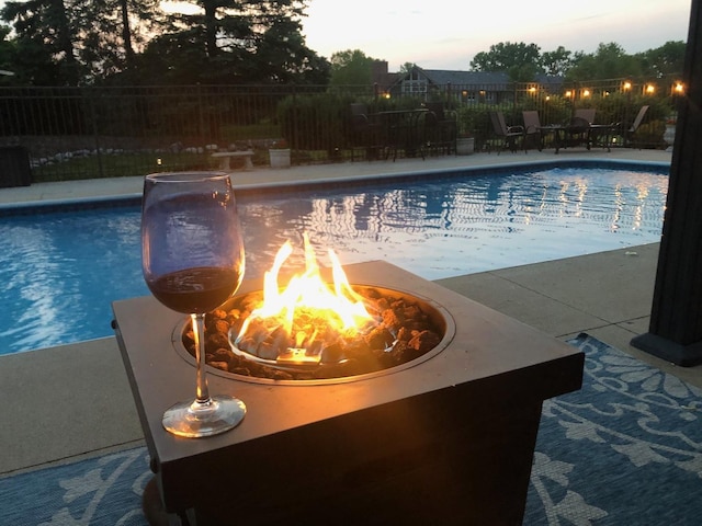 pool at dusk with a patio area, an outdoor fire pit, fence, and a fenced in pool