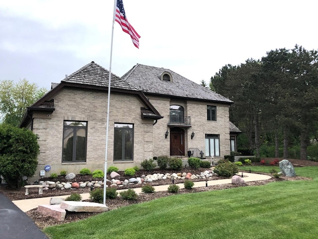 french country inspired facade with a front lawn, a balcony, and brick siding