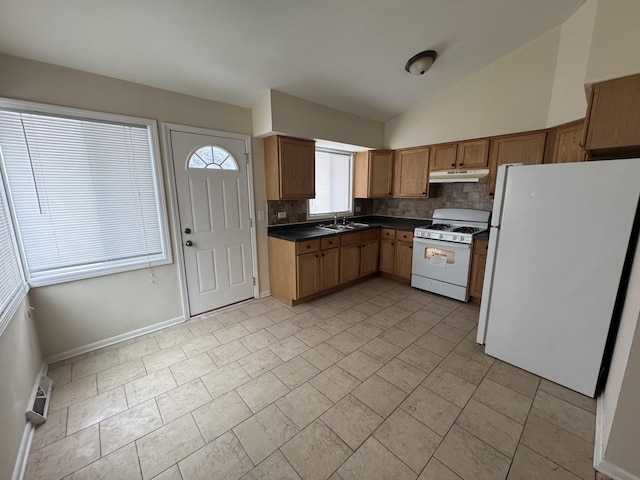 kitchen with white appliances, brown cabinetry, dark countertops, under cabinet range hood, and a sink