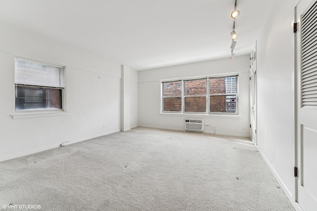 spare room with rail lighting, baseboards, carpet flooring, and a wall mounted AC