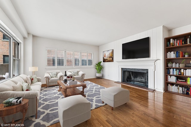 living room featuring a fireplace with raised hearth, baseboards, and wood finished floors