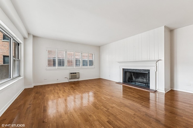 unfurnished living room featuring wood finished floors, a fireplace with raised hearth, and a wall mounted AC