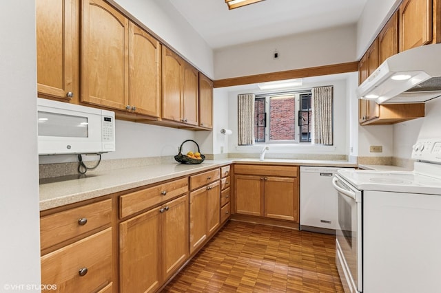 kitchen featuring white appliances, brown cabinetry, light countertops, under cabinet range hood, and a sink