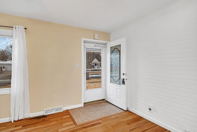 interior space with brick wall, light wood-style flooring, visible vents, and baseboards