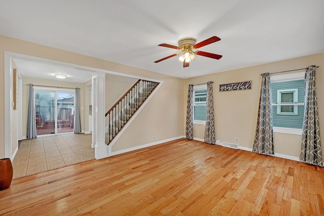 empty room with visible vents, stairway, light wood-style flooring, a ceiling fan, and baseboards