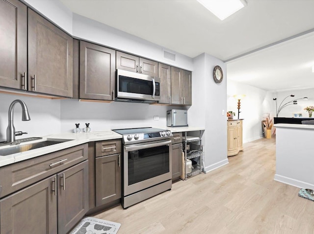 kitchen featuring appliances with stainless steel finishes, light countertops, dark brown cabinets, light wood-type flooring, and a sink