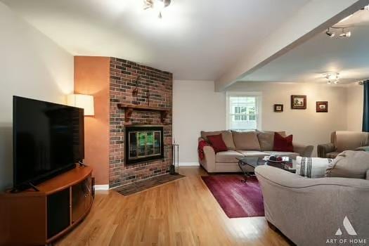 living area with a brick fireplace, baseboards, beam ceiling, and wood finished floors