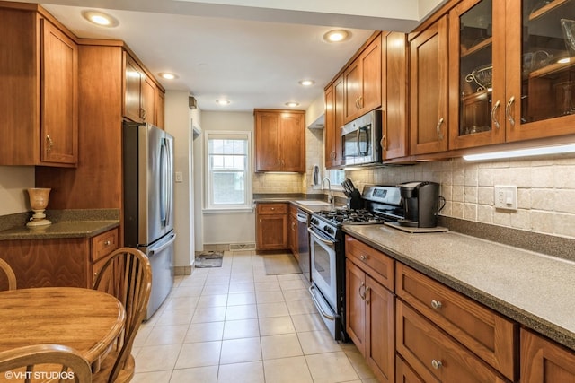 kitchen with stainless steel appliances, brown cabinets, glass insert cabinets, and light tile patterned flooring