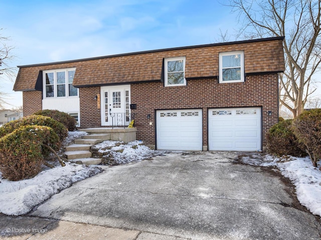 bi-level home with brick siding, mansard roof, a shingled roof, an attached garage, and driveway