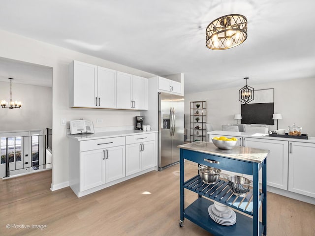 kitchen featuring white cabinetry, light countertops, stainless steel refrigerator with ice dispenser, light wood finished floors, and pendant lighting