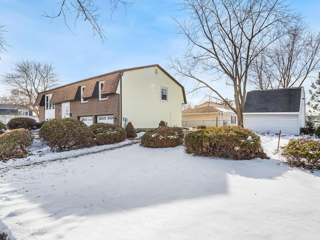 snow covered property with a garage, a shingled roof, and a gambrel roof