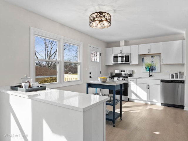 kitchen with light wood finished floors, stainless steel appliances, light countertops, white cabinetry, and a sink