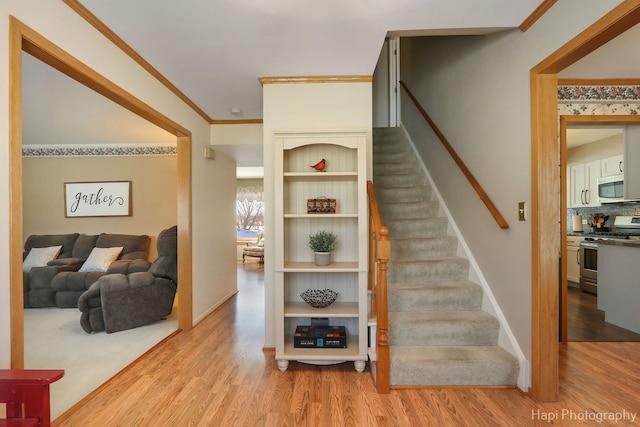 staircase with ornamental molding, wood finished floors, and baseboards