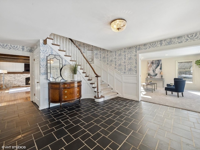 entryway featuring wallpapered walls, stairway, a decorative wall, and wainscoting