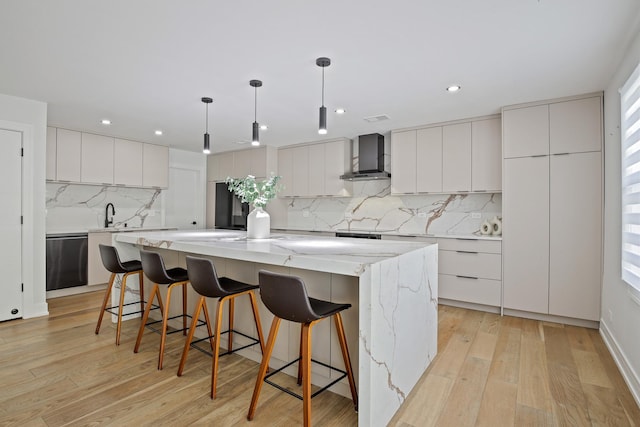 kitchen featuring a spacious island, a kitchen breakfast bar, wall chimney range hood, light wood-type flooring, and dishwasher