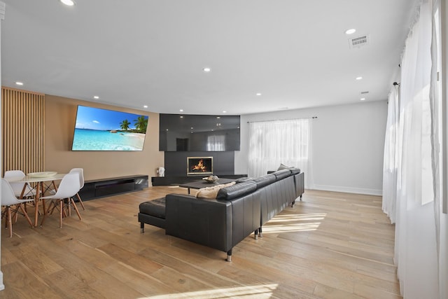 living room with a warm lit fireplace, light wood-type flooring, visible vents, and recessed lighting