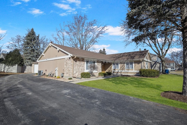 view of front facade with aphalt driveway, cooling unit, a garage, stone siding, and a front yard