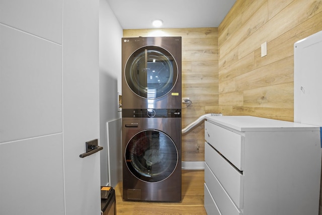 washroom with light wood-style floors, stacked washer and clothes dryer, wooden walls, and laundry area