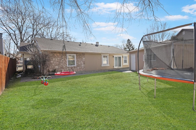 rear view of house with stone siding, a trampoline, fence, and a lawn