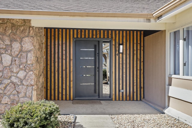 view of exterior entry featuring a shingled roof