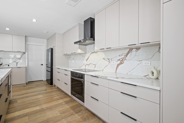 kitchen featuring white cabinetry, visible vents, light wood-style floors, wall chimney range hood, and black appliances